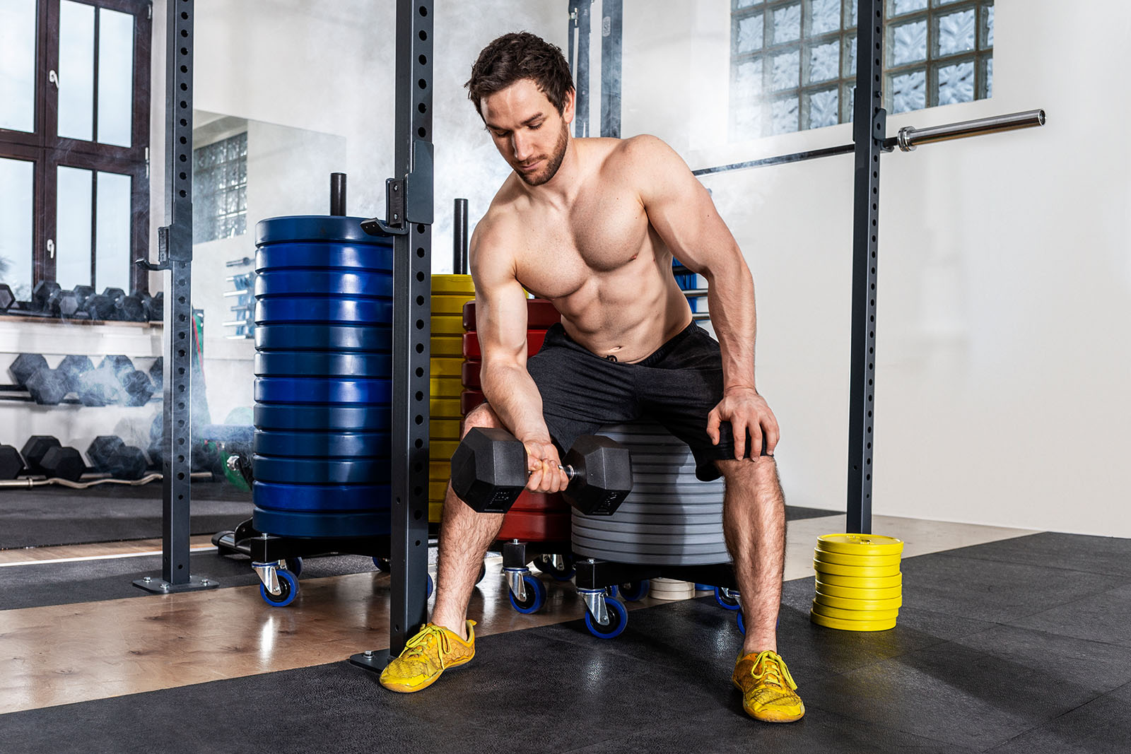 Sportler im Fitnessstudio. Ein Mann ist zu sehen, mittleres Alter. Er sitzt und greift nach einer Hantel.