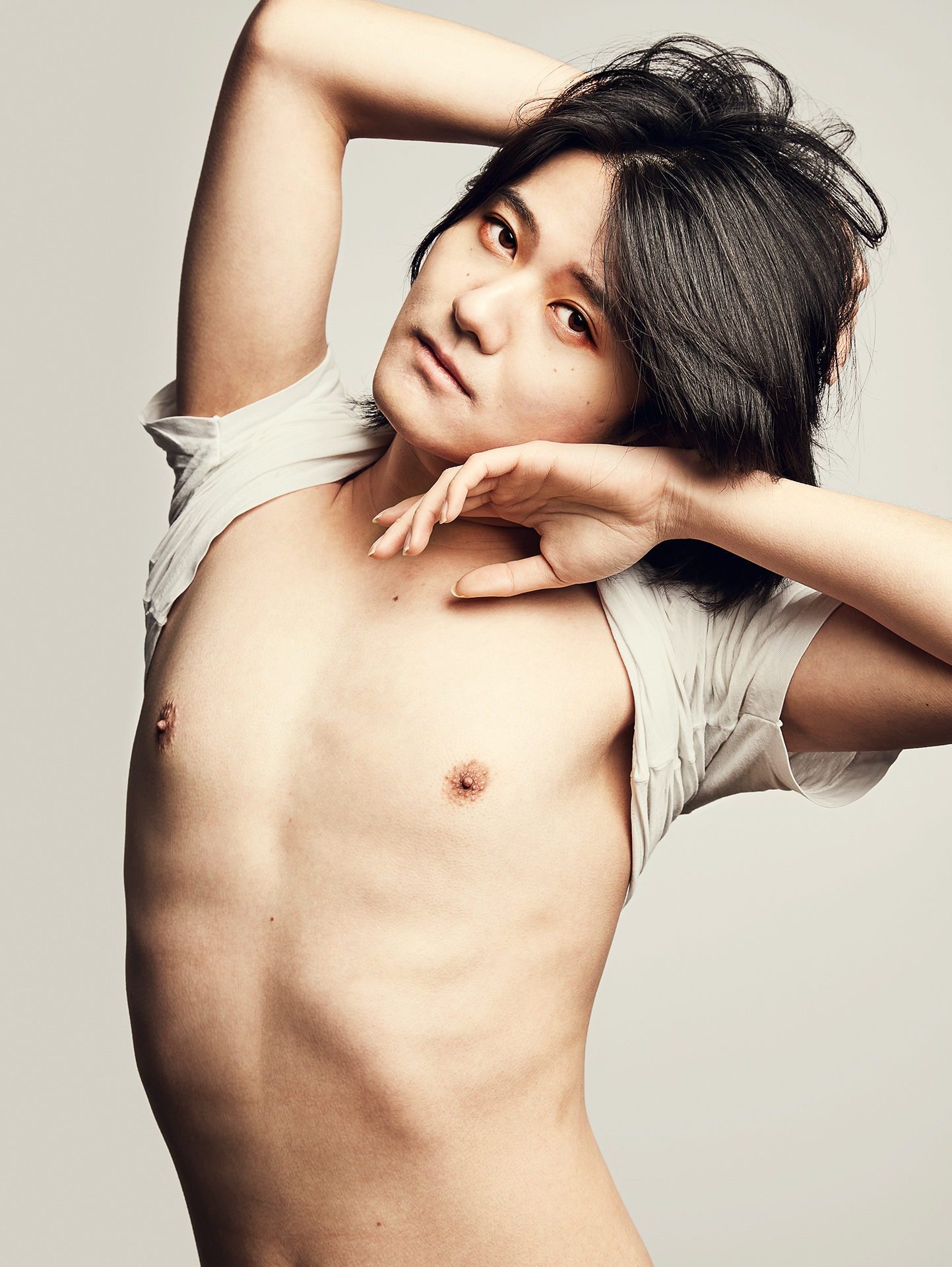 Person in weissen Tshirt posiert seitlich vor beigem Hintergrund.