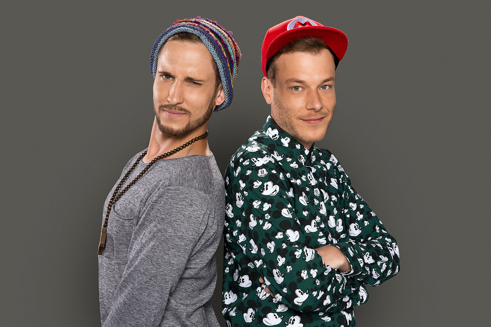 Zwei Männer der Band 257ers aus Essen stehen Rücken an Rücken vor grauem Hintergrund. Der linke trägt ein graues Langarmshirt, eine lange Holzkette und eine bunte Strickmütze, er zwinkert in die Kamera. Der rechte trägt ein Hemd mit Mickey-Mouse-Muster und eine rote Baseballkappe, er blickt lächelnd nach vorne.